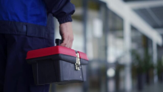 Man carries toolbox and multimeter tester. Electrician goes to repair light in office. Master finishes work on electricity. Male mechanic in uniform.