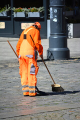 Ludzie w pomarańczowy kombinezon sprzątają miasto. 