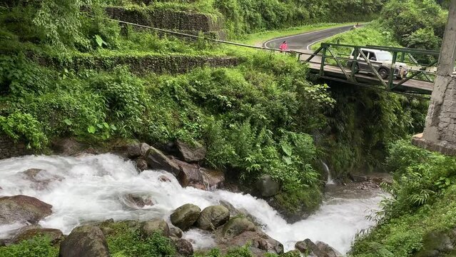 Beautiful waterfalls near a bridge with a car passing by a person in Dooars, India. Scenic beauty of Dooars landscape, West Bengal, India