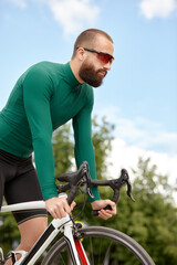 Obraz premium Man in sunglasses speeds along the road against a background of summer park. Man with a bicycle hobby rides in the park.