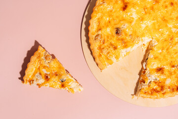 Piece cut from whole pie on wooden board on pink background.