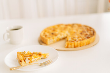 Piece of cake on white plate with fork next to cup of tea on white background.