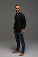 Fototapeta premium An attractive white man in jeans and black shirts tands in full growth against a gray background. Copy space