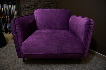 An exhibition of a stylish comfortable violet velour armchair displayed for sale, against loft brick wall background in a furniture design studio