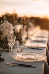 The delicate decor of the wedding banquet table in pastel colors. Wildflowers, crystal glassware, candles. Сrystal chandelier on top, illuminating the table. Rays of the setting sun.