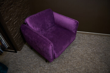 An exhibition of a stylish comfortable purple velour armchair displayed for sale, against loft brick wall background in a furniture design studio