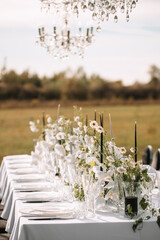 The delicate decor of the wedding banquet table in pastel colors. Wildflowers, crystal glassware, candles. Сrystal chandelier on top, illuminating the table.