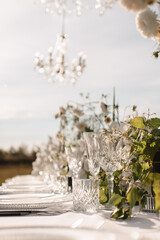 Decor for a wedding ceremony in a picturesque meadow. Wildflowers, crystal glasses, crystal plates, beautiful wedding tableware