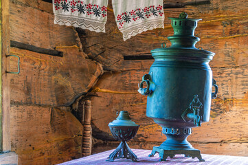 An old dark samovar and an oil lamp on a table in a rustic log house built in the 19th century. The...