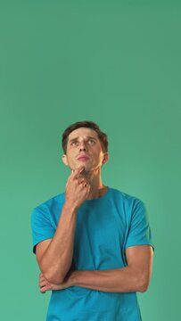 Thoughtful man. Create idea. Ponder information. Project brainstorming. Young pensive guy looking up holding chin hand isolated on green vertical copy space.