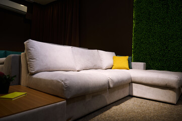 Angle view. Modern upholstered gray sofa with green and yellow cushions and journal table with a catalogue, displayed for sale in furniture store