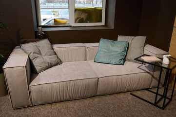 Top view of stylish comfortable sofa upholstered with light velour fabric with colorful pillows and small journal table