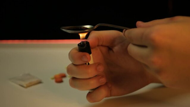 Close up of male caucasian hands boiling black heroin with a lighter in a spoon. Close shot of lonely drug addict preparing to take another dose of forbidden substance. Man cooking heroin with flame
