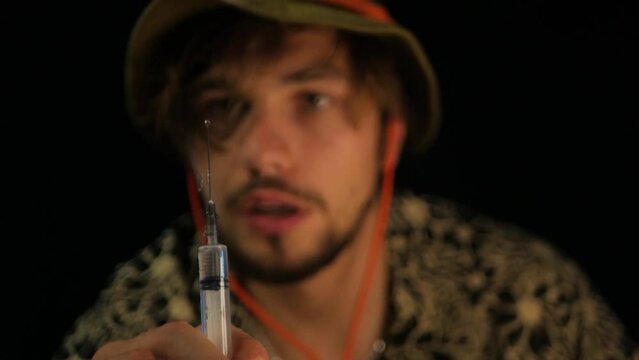 Close up of dazed man under influence of illegal substances emptying syringe. Slow motion shot of drug addicted caucasian man spraying transparent liquid from medical syringe. Concept of dependence
