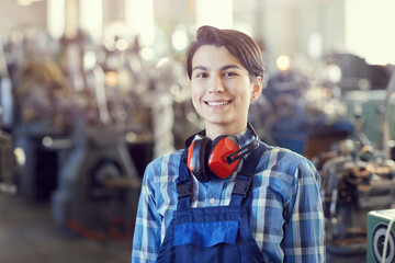 Portrait of cheerful satisfied brunette female factory worker with short hair wearing red ear...