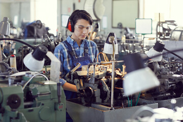 Serious concentrated young female engineer in ear protectors and safety goggles standing in factory...