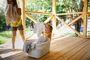 Cute European sibling children hang laundry together on veranda in backyard in summer. Helping...