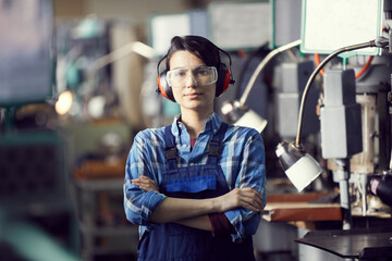 Portrait of content confident skilled young woman in ear protectors and safety goggle working at...
