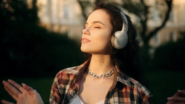 Beautiful woman dancing in a checkered shirt in a park. Free girl with long hair dance in the sunset. Healthy woman dancing outdoors. Enjoying Music