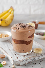 Vegan banana chocolate ice cream with chocolate glaze and sprinkles in a glass on a gray concrete background. Healthy food. Copy space.