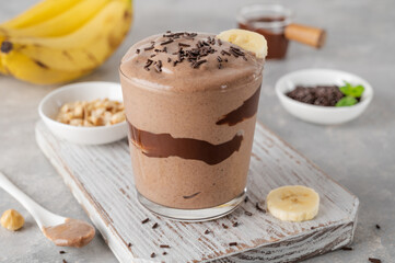 Vegan banana chocolate ice cream with chocolate glaze and sprinkles in a glass on a gray concrete background. Healthy food. Copy space.