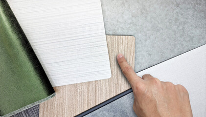 Obraz premium interior designer's hand choosing interior material samples containg green velvet fabric, white fabric laminateds, oak wood veneers and concrete vinyl flooring, close up view. mood and tone board.