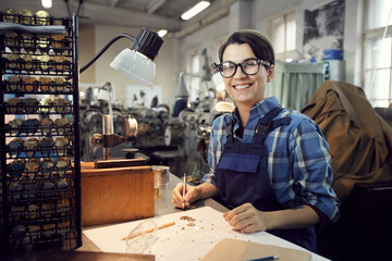 Portrait of jolly excited young woman in eyeglasses sitting at table and working with watch...