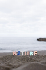 Word nature made of colourful wooden letters stand on the beach in front of the ocean.