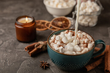 Cup of tasty cocoa drink and marshmallows in a blue cup.Pouring milk in cocoa.Spices and marshmallows for winter drinks on a black texture table.Winter hot drink.