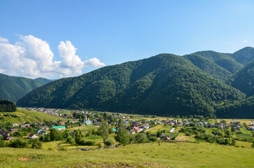 Fototapeta na wymiar Picturesque rural landscape of a green valley and a village at the foot of a mountain range densely overgrown with forest on a sunny summer day. Kolochava, Carpathian Mountains, Transcarpathia, Ukrain