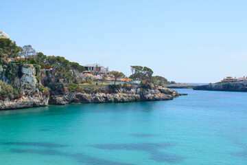 Houses on top of the coastal cliffs in Porto Cristo. Calm, turquoise sea water.