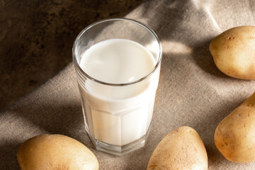 Glass of drink from potato, potato tubers on burlap. Non dairy alternative milk. Selective focus.