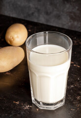 Glass with vegetable potato milk and potato tubers on old rusty metal surface close up.
