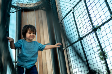 a three-year-old boy is playing in a summer park on a playground, he is climbing an alpine grid,...