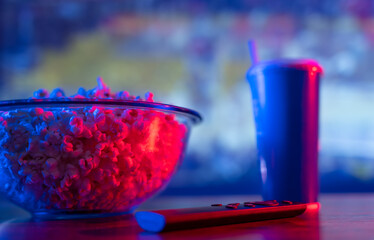 Close-up. Popcorn in a glass bowl, lemonade in a glass and a TV remote with a sports program in the...