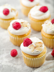 Lots of muffins with whipped cream, fresh red raspberries and almond pieces on a white background. Lots of objects. Festive food, banquet, picnic. Advertising, banner, invitation.