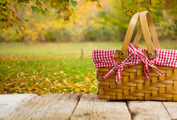 On a wooden table a straw picnic basket against the backdrop of autumn nature. Golden autumn leaves...