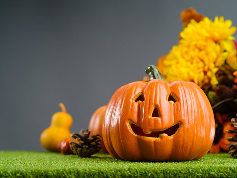 Funny orange pumpkin with a smile, autumn fruits, cones and flowers on green grass on a gray background. Halloween composition. Favorite holiday for children.