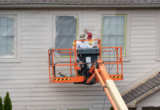 Two home painters in articulating boom lift spray painting townhouse