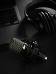 Close-up. On a dark gray background, a studio microphone, studio headphones on an open laptop....