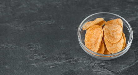 Potato chips in glass bowl on dark background. Fast food.