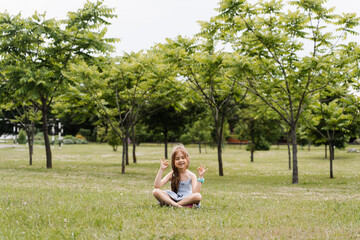 Adorable child girl is sitting and meditate in lotus pose in the park. Relaxation and meditation of kids outdoor. Lifestyle of calm toddler. Enjoy life.