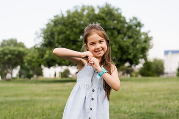 Fototapeta premium Adorable child girl showing heart with her hands. Cute toddler shows peace and love. Happy kid smiling and posing in green park.