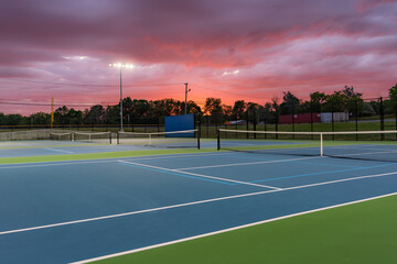 Evening photo of outdoor blue tennis courts with pickleball lines with lights turned on.	