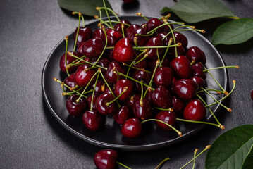 Fresh sweet cherries plate with leaves in water drops on stone background, top view