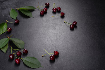 Fresh sweet cherries plate with leaves in water drops on stone background, top view
