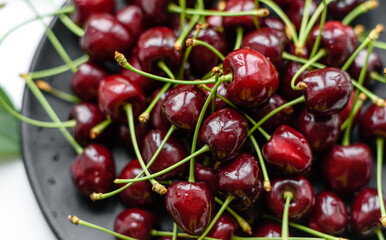 Fresh sweet cherries plate with leaves in water drops on stone background, top view