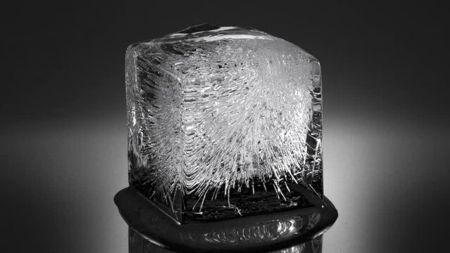 Melting ice cube, water flowing to foreground (viewer). Long version. 