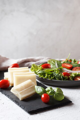 A piece of fresh sliced halloumi on a slate board with cherry tomatoes and spinach leaves. Preparing to cook cheese on the grill. Copy space.