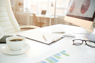 Close-up of modern workplace with financial papers, coffee and computer with graphs on screen in office